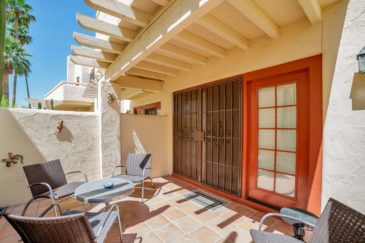 A cozy outdoor seating area adjacent to a decorative wall and entrance door, offering a comfortable spot for relaxing or socializing outdoors. The scene is framed by attractive landscaping, enhancing its inviting, tranquil atmosphere.