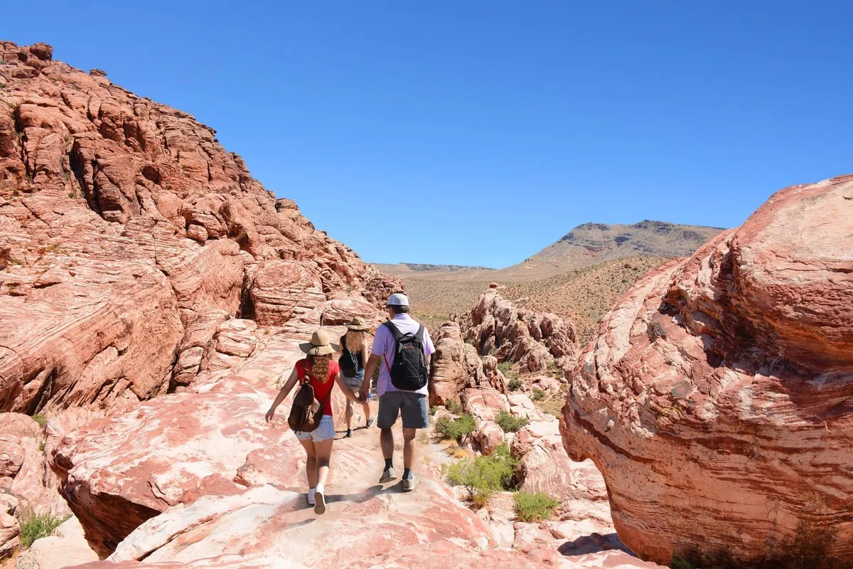 Red rock formations rise dramatically under a clear blue sky, with hikers navigating the terrain. The scene inspires excitement and highlights the region’s opportunities for family adventure and exploration.
