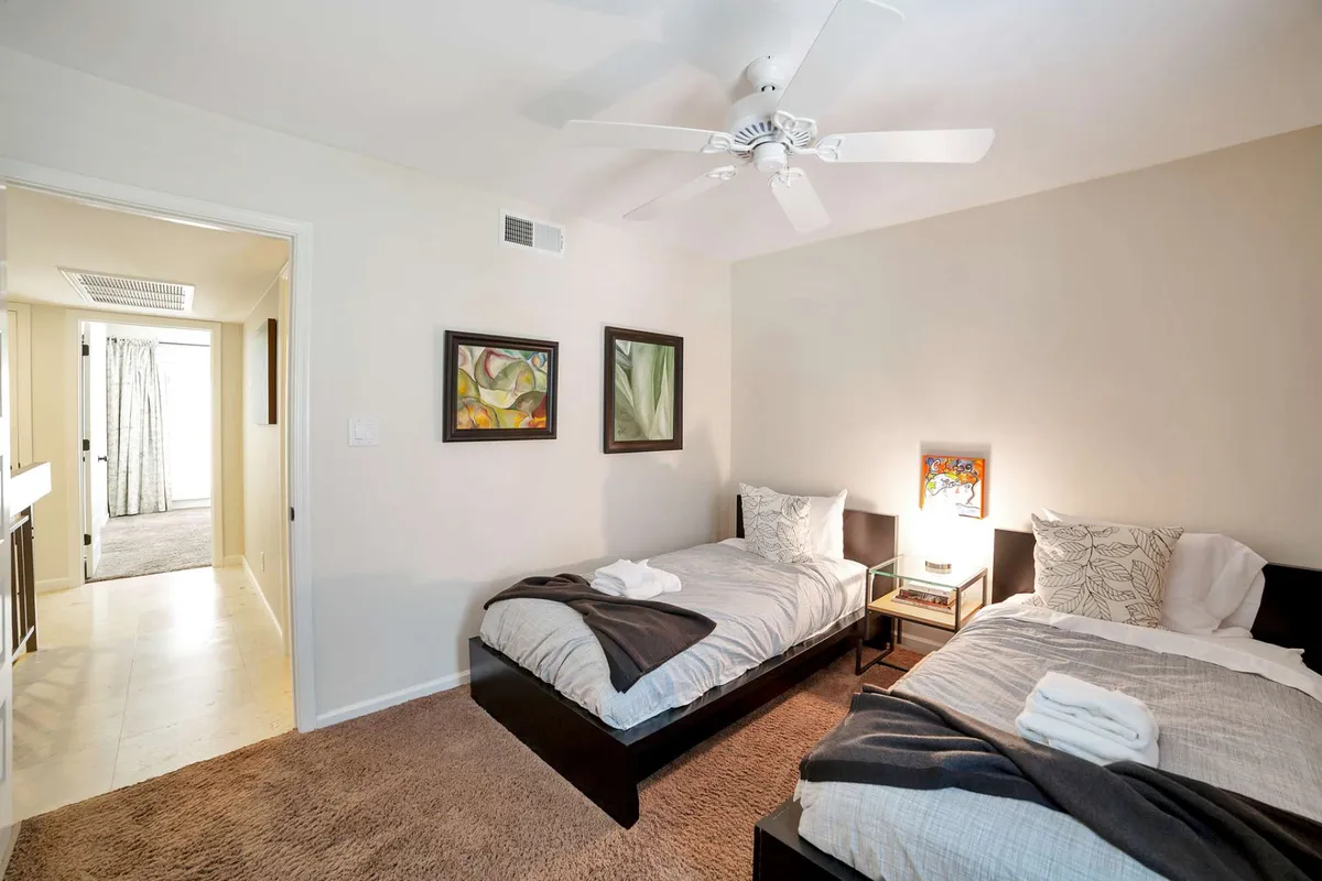 A guest bedroom outfitted with two twin beds, each neatly made, complemented by colorful artwork on the wall and a shared nightstand with a lamp. The mood is relaxed and inviting, perfect for families or friends.