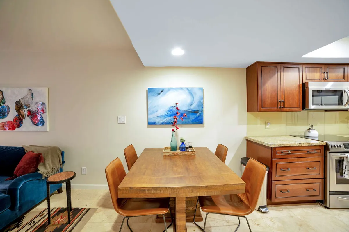 This image features a cozy dining nook with a wooden table and seating for four, alongside colorful artwork and a glimpse of the kitchen's cabinetry. The arrangement invites group meals, conversation, or planning activities.