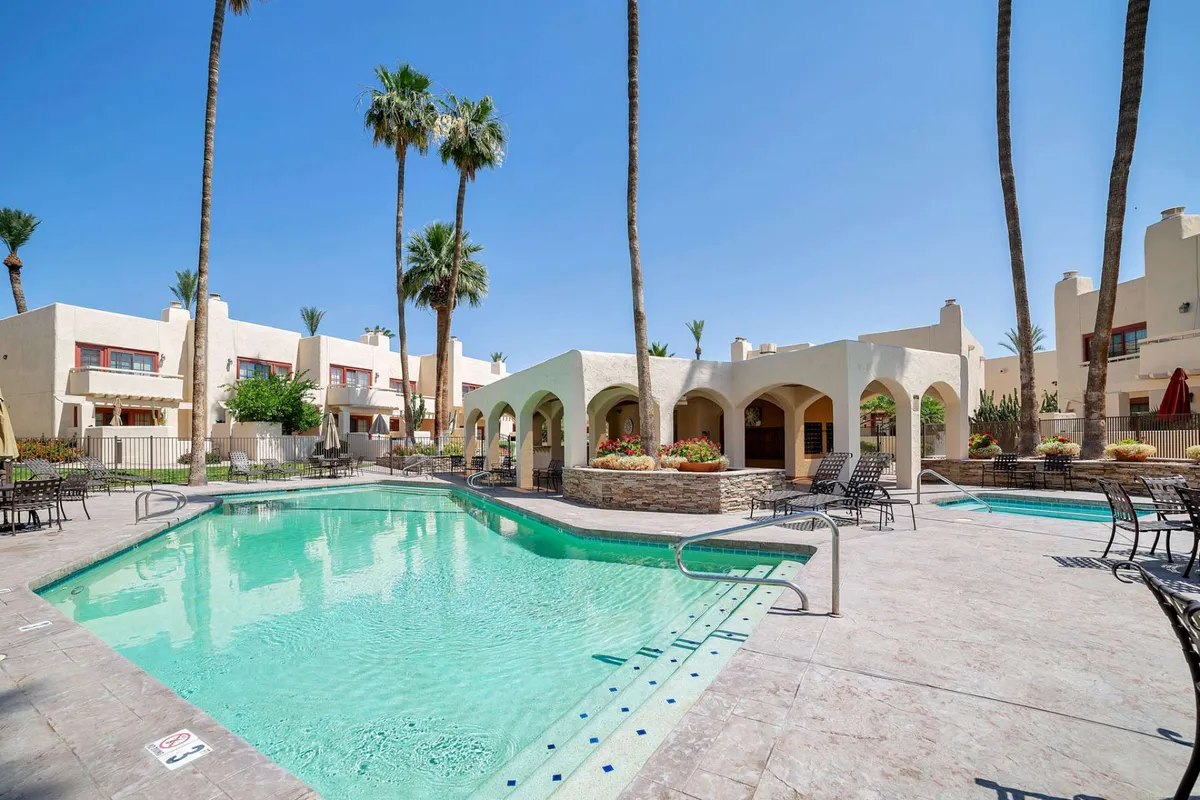 This vibrant exterior image centers on a sparkling swimming pool bordered by palm trees and a stylish arched structure, with outdoor seating areas that encourage social gatherings. The lively scene suggests both activity and relaxation, evoking the feel of a resort getaway.