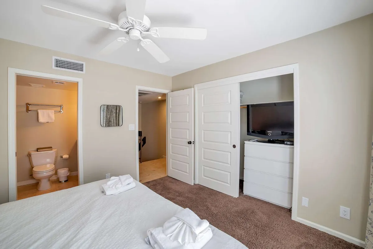 A serene bedroom scene with a neatly made bed, towels arranged for guests, and open doors leading to a bathroom and another room, suggesting easy flow and access. The setting is calm, ideal for rest after a day of exploring or outdoor activities.