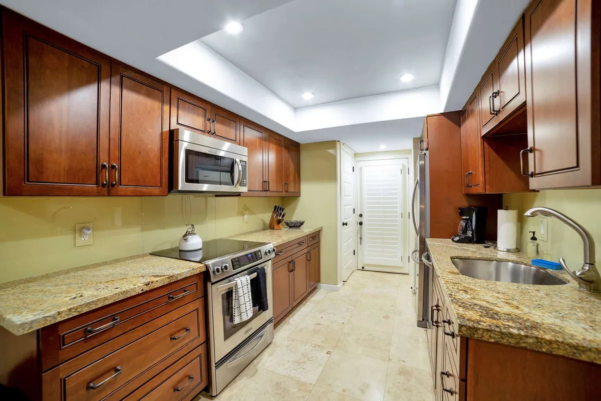 The modern kitchen features a granite countertop, wood cabinetry, and updated stainless steel appliances, all illuminated by warm lighting. The spacious counter suggests ample room for preparing meals, morning coffee, or quick snacks between meetings.